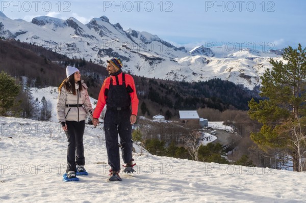 Couple snowshoeing hand in hand through fresh pyrenees snow, smiling and enjoying a sunny winter