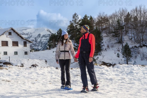 Happy couple holding hands while snowshoeing on a sunny winter day, enjoying active leisure time in
