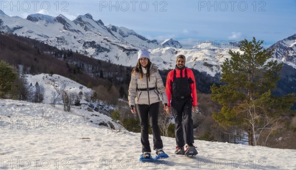 Couple snowshoeing on a snowy mountain trail, smiling and looking at the camera, with majestic snow