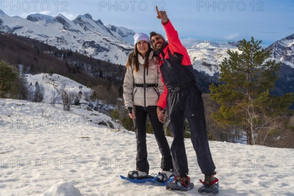 Young couple enjoying outdoor winter adventure, snowshoeing in a snowy mountain landscape under