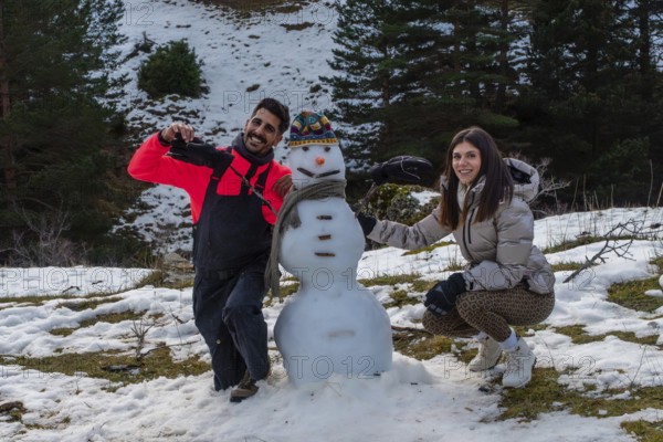 Couple building a snowman together on a snowy mountain slope, smiling and bundled in winter gear,