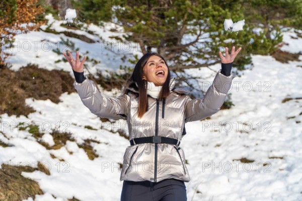 Young woman dressed in a warm jacket joyfully celebrating the outdoor winter season by throwing
