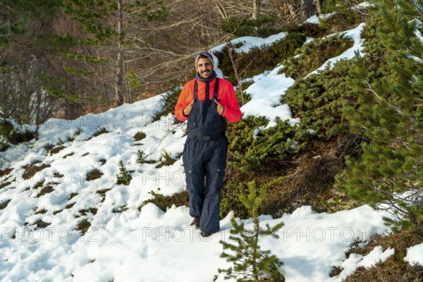 Man in an orange sweater and dark bib pants smiling, enjoying winter nature while walking through a