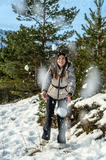 Young woman smiling and catching falling snow in a sunlit pine forest on a mountain winter