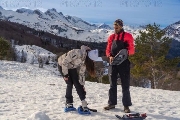 Young couple actively preparing snowshoes on a sunny winter day, ready for a trekking adventure in