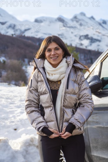 Young woman smiling while zipping up her warm jacket, standing outdoors in a snowy mountain
