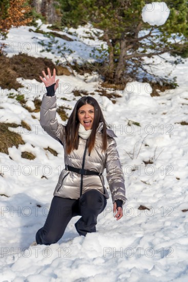 Young woman kneeling in snow with a playful expression, throwing a snowball against a backdrop of
