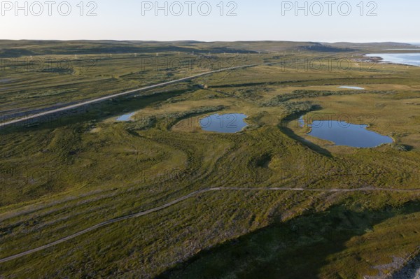 Coastal landscape on Varangerfjord with blue sky, still sea, moors and pebble beach aerial view,
