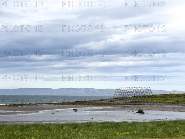 Coast with green shore, wooden racks for drying stockfish and cloudy sky over the sea, Nesseby,