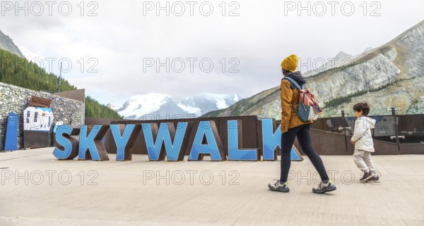 Tourists walking by large skywalk sign with athabasca glacier and mountains in background at