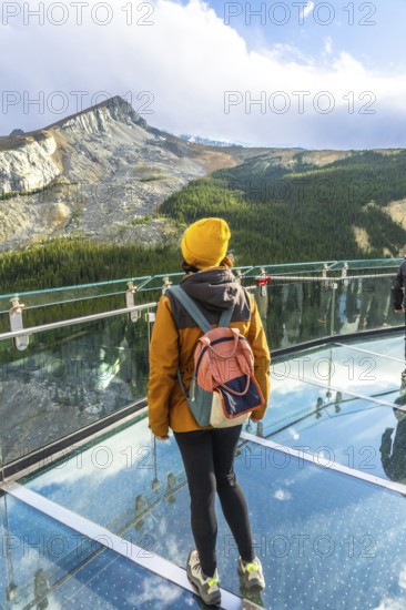 Tourist wearing yellow hat and backpack standing on the glass platform of the glacier skywalk