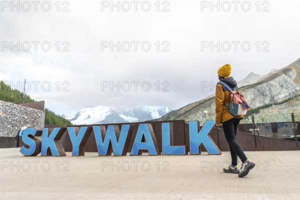 Female tourist walking near the skywalk sign with the athabasca glacier and mountains in the