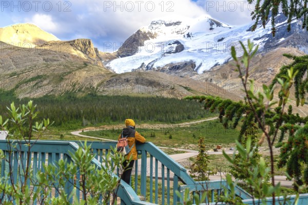 Tourist wearing a yellow beanie and jacket, leaning against a wooden fence, admiring the