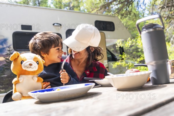 Mother and son are sitting at a picnic table, enjoying breakfast outside their campervan in banff