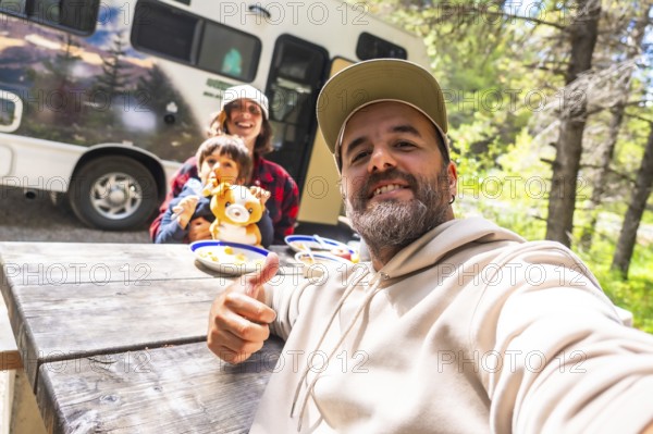 Happy family taking a selfie while having lunch on a wooden table near their camper van in the