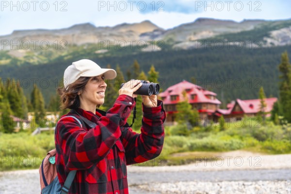 Female tourist using binoculars enjoying the landscape at bow lake with the iconic num ti jah lodge