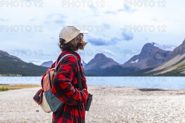 Young hiker standing on the shore of turquoise bow lake, contemplating the majestic mountains of