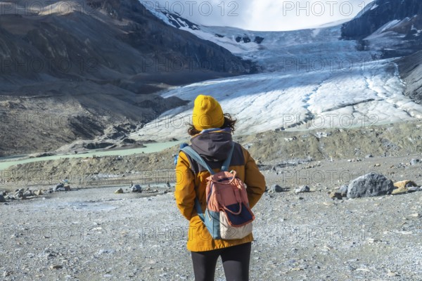 Female hiker in a yellow jacket and backpack admiring the majestic athabasca glacier in jasper