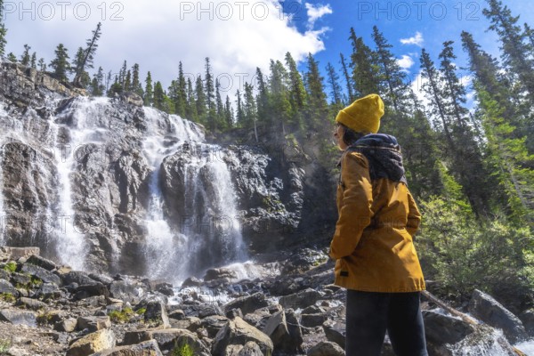 Female hiker wearing yellow beanie and jacket is admiring cascading waters of tangle creek falls in