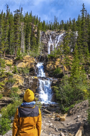 Hiker in a yellow jacket and beanie contemplating the cascading waters of tangle creek falls in