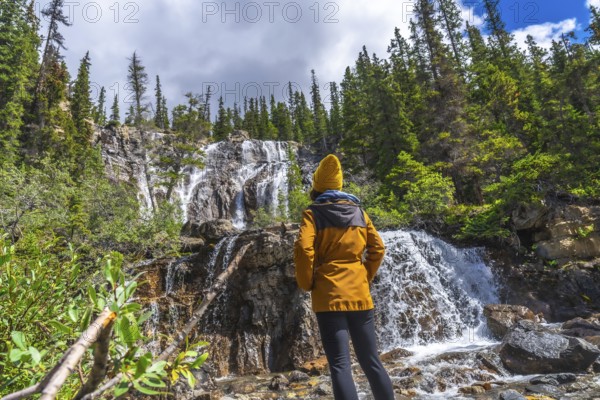 Female hiker wearing yellow jacket and beanie contemplating tangle creek falls in jasper national