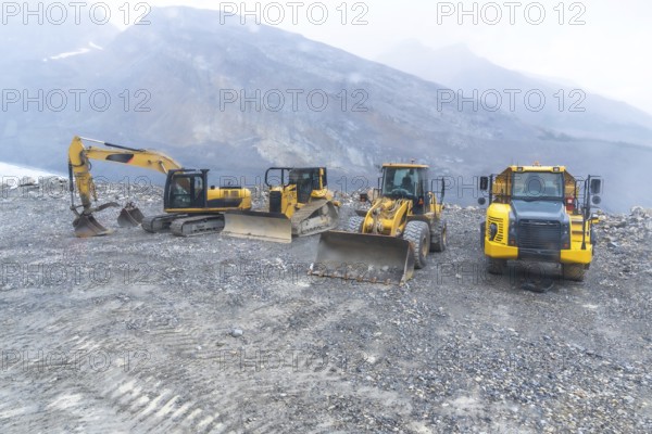 Excavator, bulldozer, and dump truck parked on gravel near athabasca glacier, highlighting