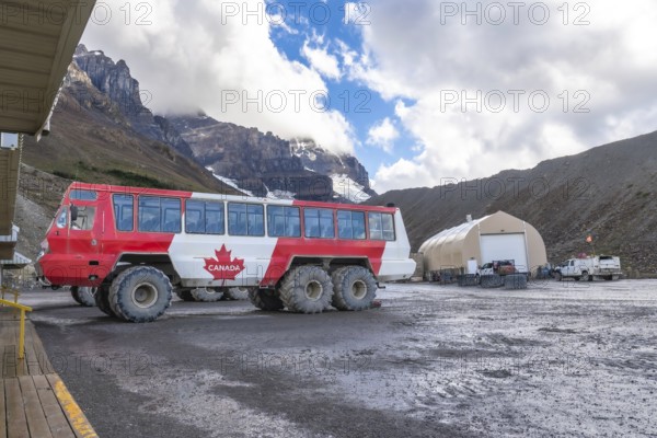 Large all terrain bus with a canadian flag parked near athabasca glacier in columbia icefield,