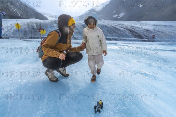 Mother and child enjoying playful moments on the athabasca glacier, with a toy vehicle in the