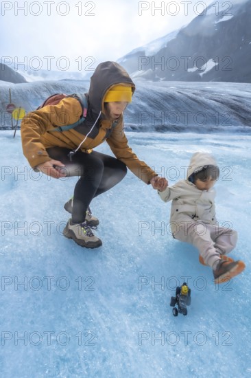 Tourist mother helping her child after slipping on the ice surface of the athabasca glacier in