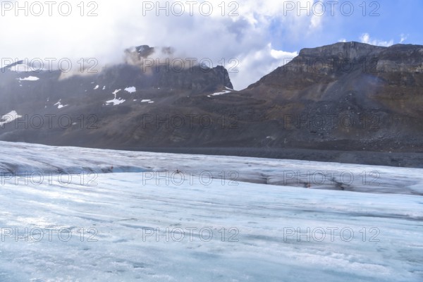 Tourists walking on the athabasca glacier in jasper national park, surrounded by mountains and