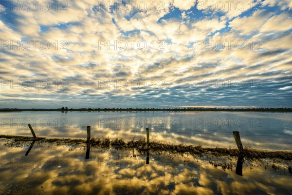 Sky with dramatic clouds is reflected in calm water at sunset, creating a peaceful and impressive