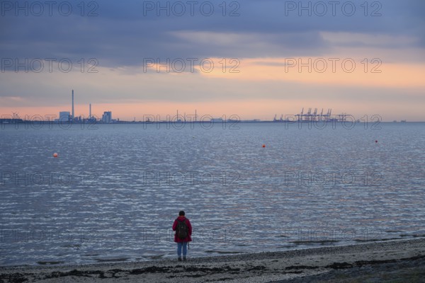 Person on the beach with a view of the sea and industrial areas in Wilhelmshafen right Jade-Weser