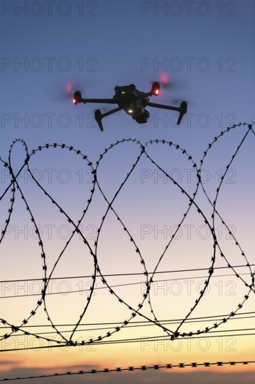 Icon image, illuminated drone hovering over barbed wire at late sunset, airport, threat, espionage