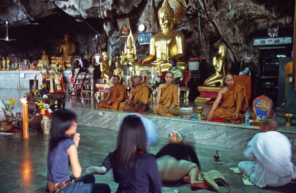 Buddha statue, monks and believers praying, Wat Tam Sua monastery near Krabi, Thailand, December