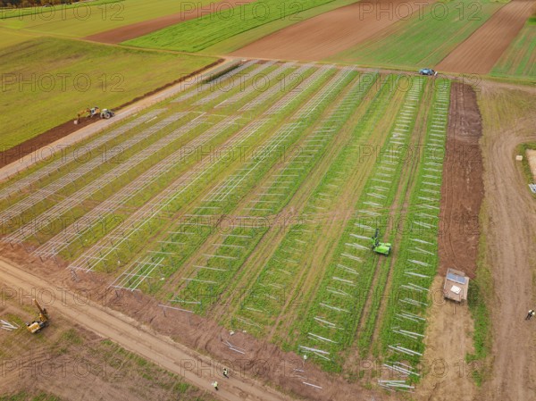 Green field with commencing construction of solar systems, tractors in use, energy transition,