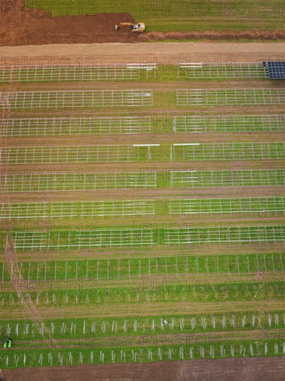 Aerial view of green fields with beginning solar plant construction and agricultural patterns,