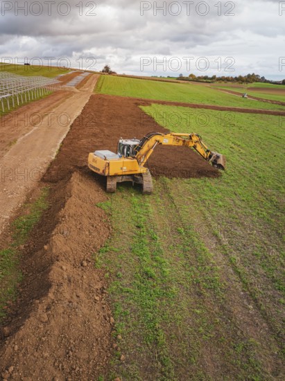 Excavator moves soil over a wide field under cloudy sky, Energiewende, construction of PV open