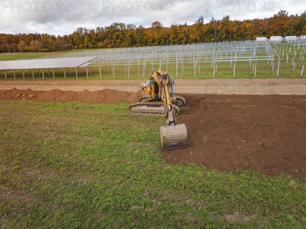 Excavator working near solar panel structures with autumn leaves in the background, energy