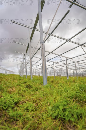 Close-up of metallic solar frames in the construction phase on a green field under cloudy sky,
