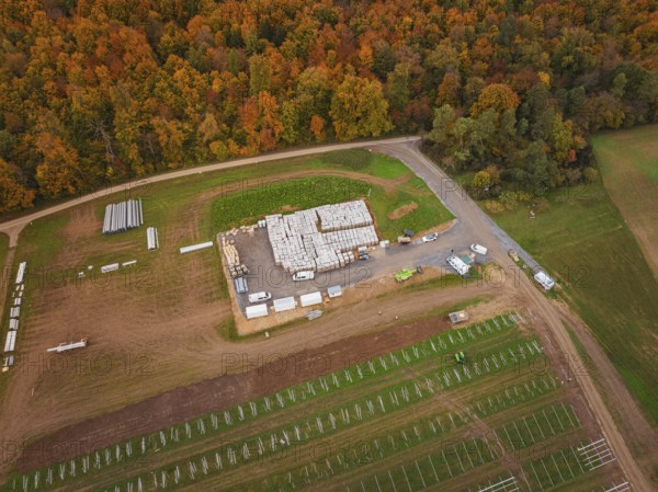 Large-scale warehouse with building materials and vehicles, surrounded by autumn landscape and