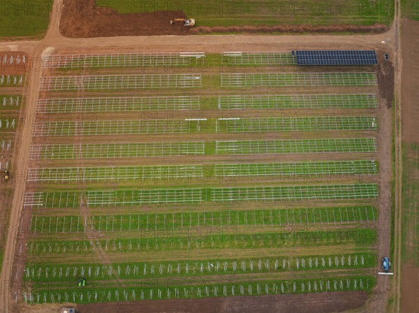 Large-scale solar frame construction on a field, surrounded by farmland seen from the air, energy