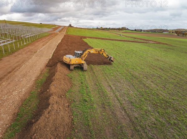 Yellow excavator shovels soil and redesigns the field, energy transition, construction of PV open