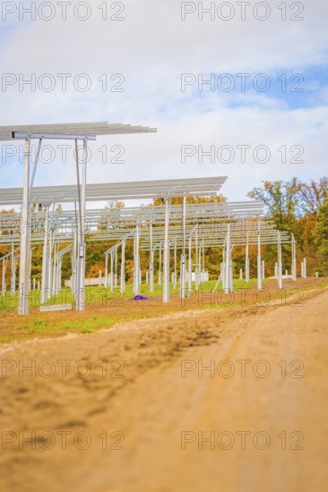 Unpaved road leads past metal structures for solar panels under blue sky, Energiewende,