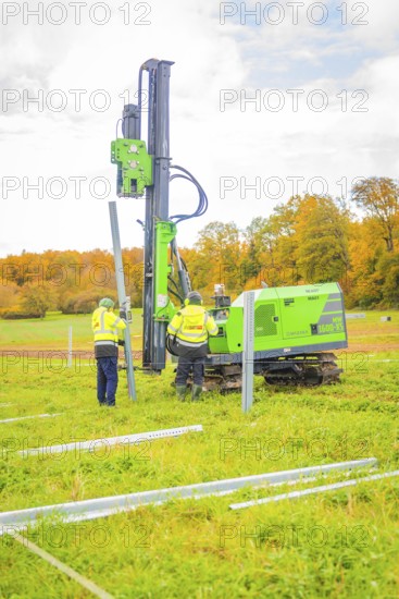 Two workers set up posts in a meadow with a drilling rig, Energiewende, construction of PV open