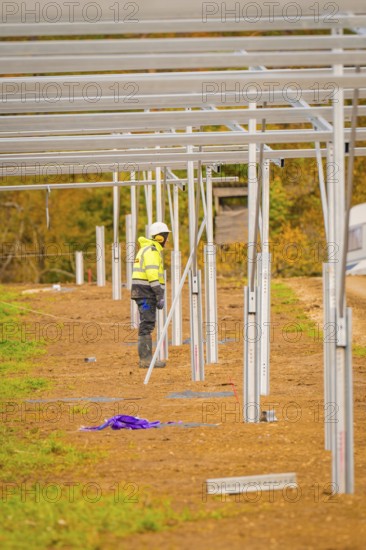 Craftsman in safety clothing working on the construction of solar panels in an open field,
