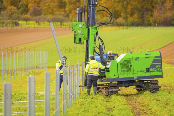 Green machine and worker installing metal poles in the field on a sunny autumn day, Energiewende,