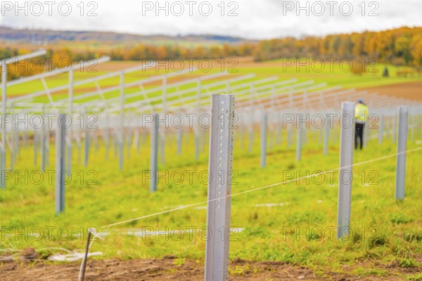 Metal poles along a field under cloudy sky with autumn landscape in the background, Energiewende,
