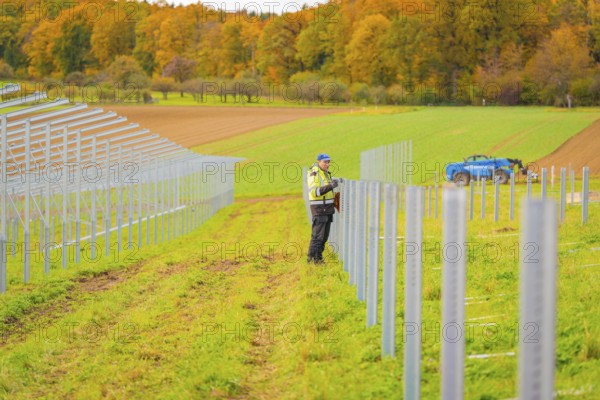 A worker installs poles in a field on a clear autumn day, Energiewende, construction of PV open
