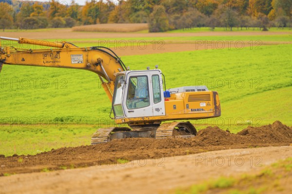 Large yellow excavator operating on an open, green area, energy revolution, construction of PV open