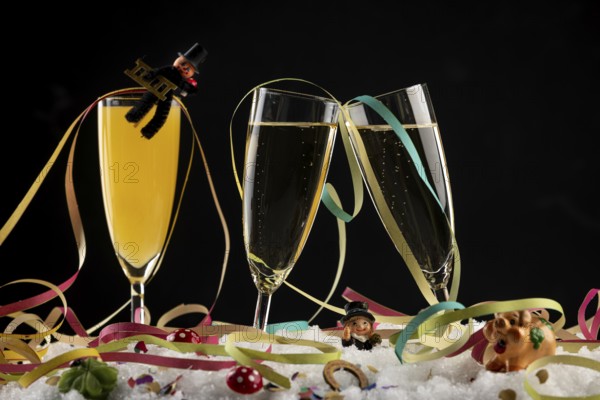 Three champagne glasses with lucky charms for the New Year and streamers in the snow